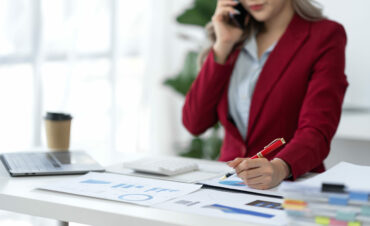 Attractive Asian businesswoman using mobile phone to search, contact, chat, business negotiations with customers. Online paperwork at office desk.
